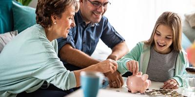 Man and woman watch child add coins to piggy bank