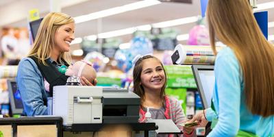 Woman holding a child while young girl pays for groceries