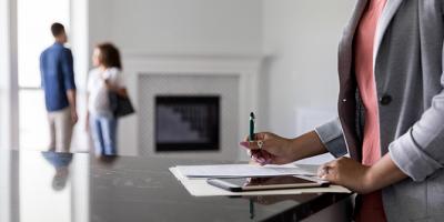 Real estate agent finishes paperwork on home purchase, couple talking in the background.