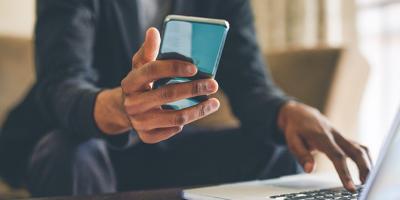 Right hand holding cell phone with left hand on laptop