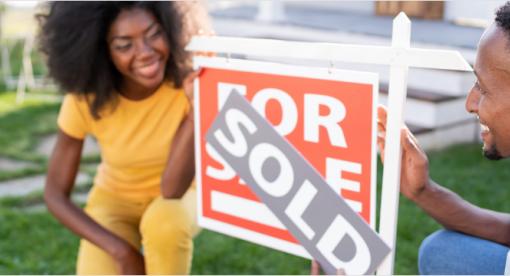 Couple kneeling next to a home sold sign.