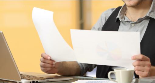 Man sitting a desk comparing two pieces of papers.