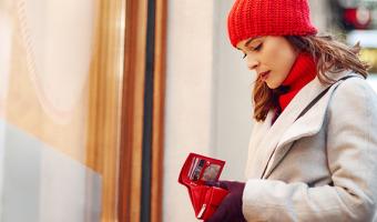 Woman standing outside store looking into wallet