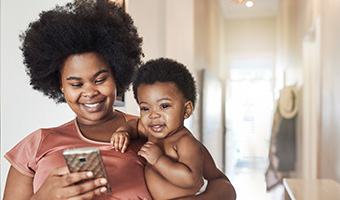 Young mom checks her cellphone while holding her baby.