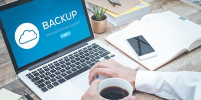 The word backup on a laptop screen with hand holding cup of coffee